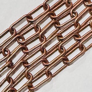 May include: A close-up of a copper chain with oval links. The chain is made of a shiny, metallic copper and has a smooth, polished finish.