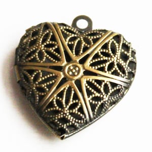May include: A gold-toned metal heart-shaped locket with a delicate filigree design. The locket has a loop at the top for hanging.