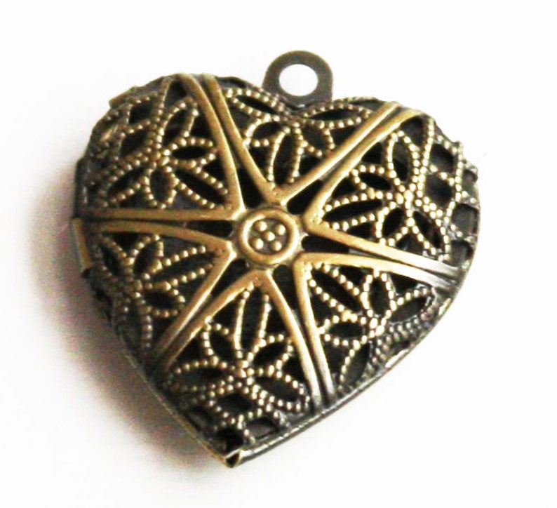May include: A gold-toned metal heart-shaped locket with a delicate filigree design. The locket has a loop at the top for hanging.