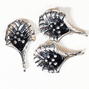 May include: Three silver flower-shaped charms with a textured surface and a small hole at the top for attaching to jewelry or other crafts.