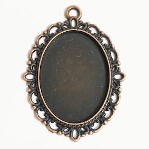 May include: A copper-toned oval pendant with a decorative filigree frame and a black, circular, blank space in the center.