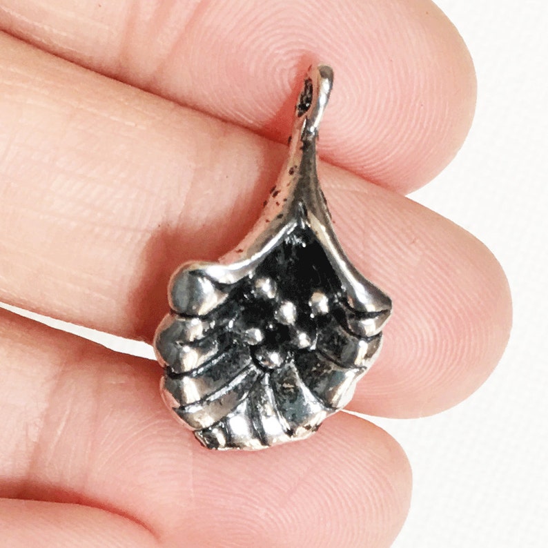 May include: Silver-toned metal charm shaped like a flower with a textured surface and a loop at the top for attaching to jewelry or other crafts.