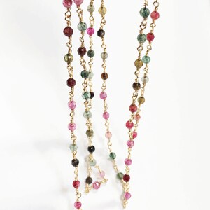 May include: A gold chain necklace with multi-colored gemstone beads. The beads are a mix of pink, green, brown, and black.