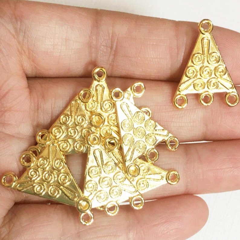 May include: Five gold-tone triangle-shaped metal connector charms with a swirl design and three holes on each side.