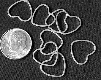 Könnte beinhalten: Eine Gruppe silberner herzförmiger Metallringe, einige überlappend, auf einem schwarzen Stoffhintergrund. Eine US-Dime-Münze ist zur Größenbestimmung enthalten.