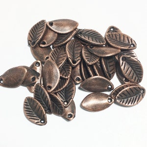May include: A pile of copper-colored metal leaf charms with a textured leaf design. The charms have a hole at the top for attaching to jewelry or other crafts.
