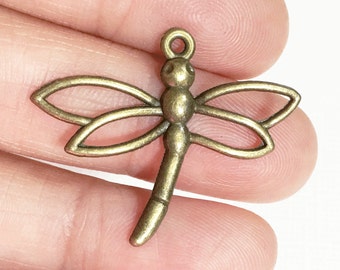 May include: A bronze-colored dragonfly charm with a loop at the top for hanging. The dragonfly has detailed wings and a long, slender body.
