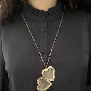 K&ouml;nnte beinhalten: Eine silberne Kettenkette mit einem herzf&ouml;rmigen Anh&auml;nger. Das Medaillon ist ge&ouml;ffnet und zeigt zwei herzf&ouml;rmige F&auml;cher.