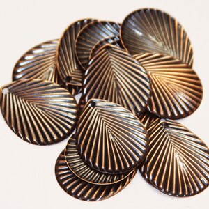 May include: A group of 10 bronze-colored metal charms shaped like seashells with a fan-like pattern. The charms have a hole at the top for attaching to jewelry or other crafts.