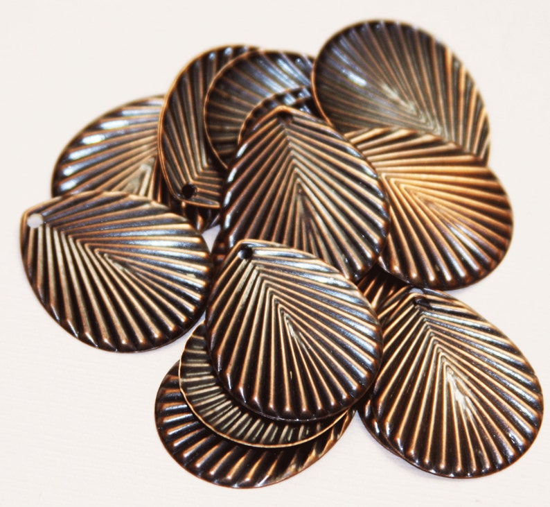 May include: A group of 10 bronze-colored metal charms shaped like seashells with a fan-like pattern. The charms have a hole at the top for attaching to jewelry or other crafts.