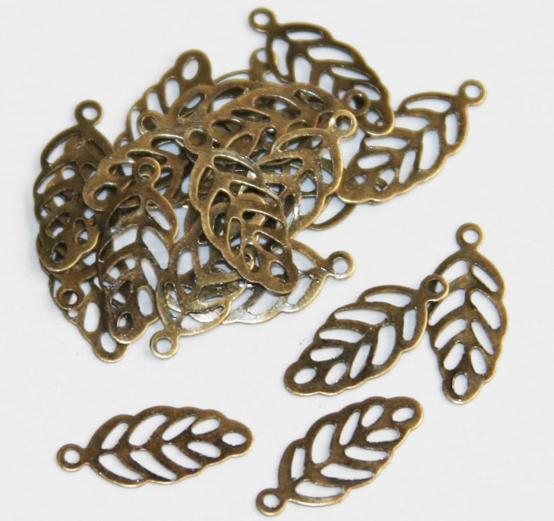 May include: A collection of antique bronze-colored metal leaf charms, each featuring a delicate filigree cutout design and a small circular loop at the top for attachment. These small, lightweight jewelry components are shaped like leaves.