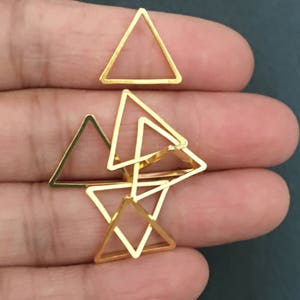 May include: A set of six gold-toned triangle-shaped metal charms. The charms are stacked on top of each other, with the largest charm at the bottom and the smallest charm at the top.