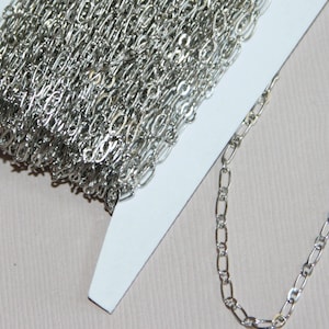 May include: A silver chain with a delicate, oval-shaped link. The chain is coiled on a white card and a section of the chain is extended to show the detail of the links.