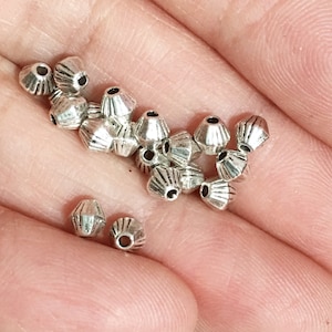 May include: A pile of silver metal beads with a decorative, fluted design. The beads are small and have a hole in the centre for stringing.