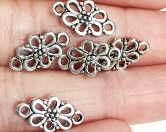 May include: Five silver-toned metal flower-shaped charms with two loops on each charm. The charms are designed with a delicate, intricate floral pattern.