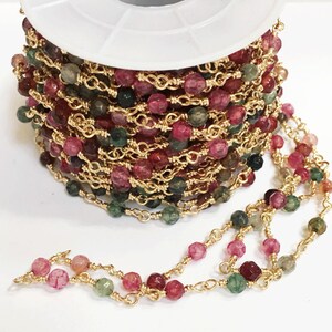 May include: A spool of gold chain with pink, green, and brown faceted beads. The chain is made of small, linked gold wire.