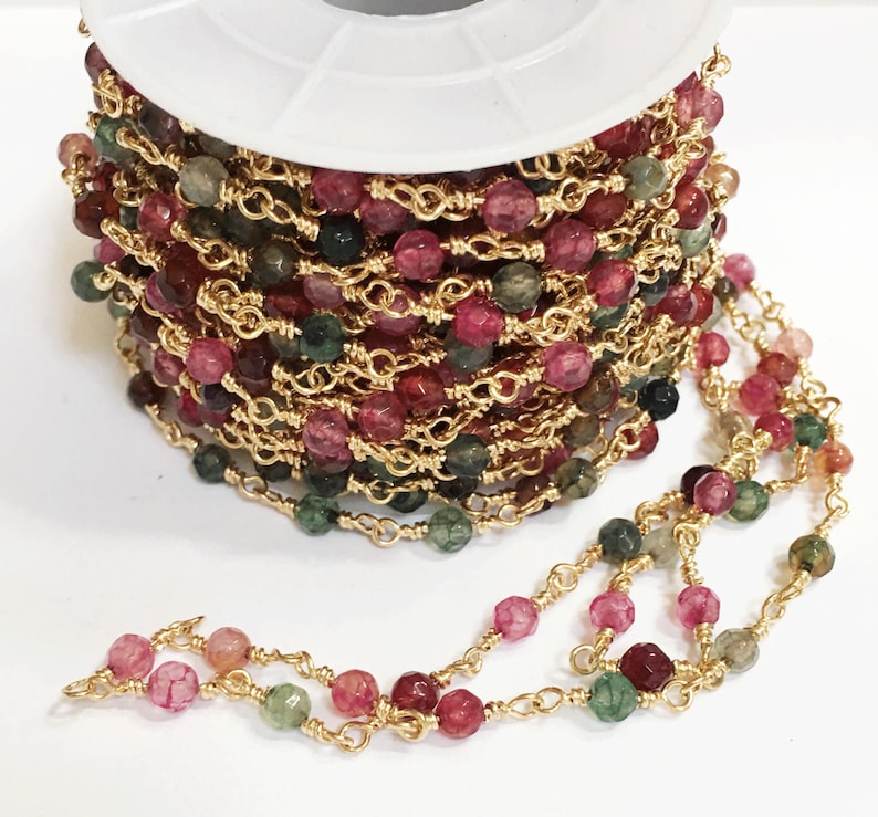 May include: A spool of gold chain with pink, green, and brown faceted beads. The chain is made of small, linked gold wire.