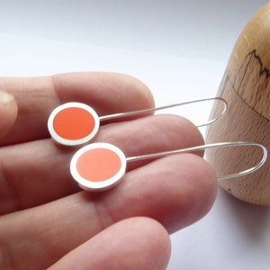 Pop orange 5 centimetres long drop earrings held in hand for scale