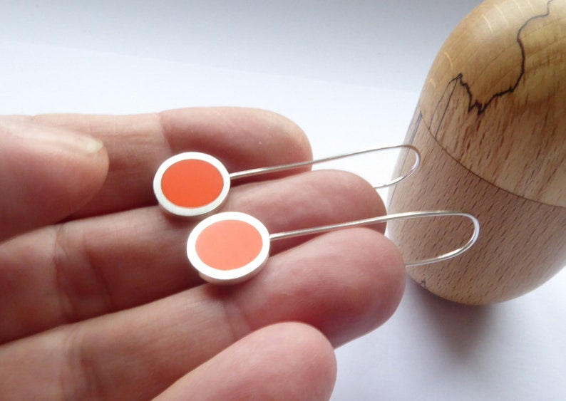 Pop orange 5 centimetres long drop earrings held in hand for scale