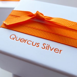 white square gift box tied with orange grossgrain ribbon with makers name Quercus Silver printed in orange on the top of the box