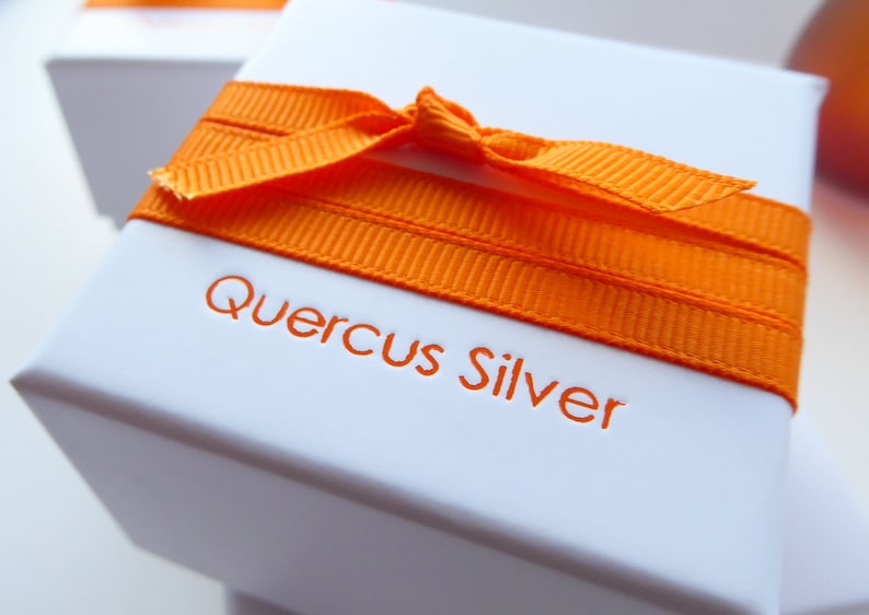 white square gift box tied with orange grossgrain ribbon with makers name Quercus Silver printed in orange on the top of the box