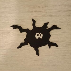 May include: Black felt patch with a spider design. The spider has eight legs and two white eyes.