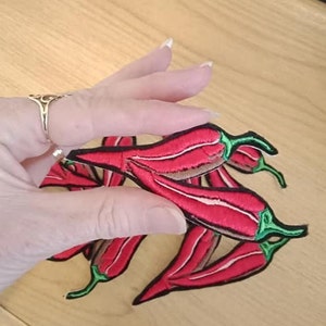 Puede incluir: Un conjunto de cinco parches de hierro de chile rojo con tallos verdes. Los parches están bordados y tienen un diseño detallado.