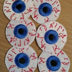 May include: Six white fabric patches with embroidered blue eyes and red blood vessels. The eyes have black pupils.