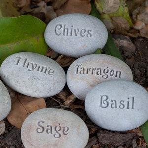 May include: A set of gray stones with the names of herbs written on them: Chives, Thyme, Tarragon, Basil, and Sage.