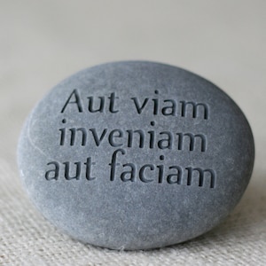 May include: A gray stone with the Latin phrase "Aut viam inveniam aut faciam" engraved on it. The phrase translates to "Either I will find a way or I will make one."