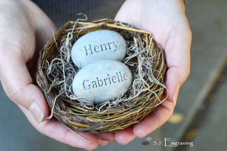 May include: Two grey stone eggs with the names "Henry" and "Gabrielle" engraved on them, nestled in a brown bird's nest.