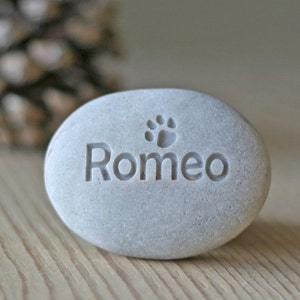 May include: A gray stone with the name "Romeo" and a paw print engraved on it.