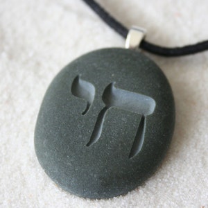 May include: A black stone pendant necklace with a silver chain and a carved Hebrew letter 'Chai' symbol.