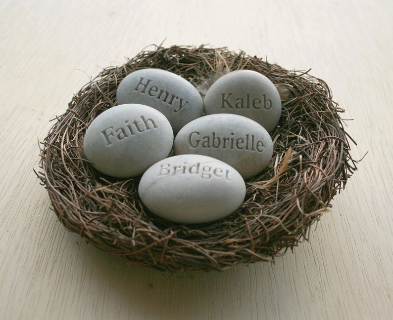 May include: Five grey stones with names engraved on them, arranged in a bird's nest. The names are Henry, Faith, Kaleb, Gabrielle, and Bridget.