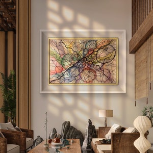 Op de afbeelding: Een woonkamer interieur met een ingelijst abstract schilderij met zwarte lijnen en kleurrijke vormen op een beige achtergrond. De kamer heeft een houten vloer, een houten salontafel, twee fauteuils, een bank en een lamp.