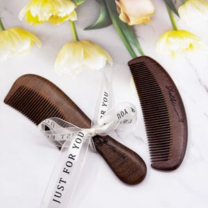 May include: Two wooden combs, one with a rounded handle and the other with a straight handle. The comb with the rounded handle has the word "Marisa" engraved on it. The comb with the straight handle has the word "Scalli" engraved on it. Both combs are tied together with a white ribbon that says "Just for you".