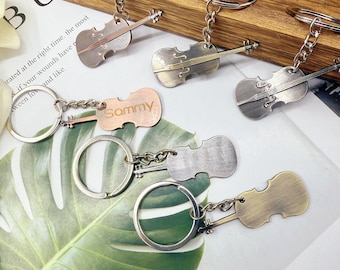 Puede incluir: Varios llaveros con forma de violín en acabados metálicos variados, incluyendo plata, bronce y cobre. Un llavero tiene el nombre "Sammy" grabado. Cada llavero tiene un anillo para llaves.