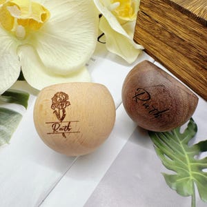 Peut inclure: Deux boîtes à bagues en bois personnalisées. L'une est de couleur claire avec une gravure de rose et le nom "Ruth". L'autre est brun foncé avec le nom "Ruth". Les deux sont en forme de demi-sphère.