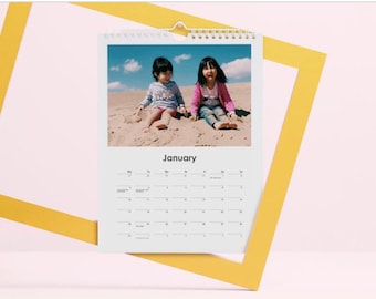 Könnte beinhalten: Ein weißer Kalender mit einem Foto von zwei jungen Mädchen, die auf einem Sandstrand sitzen. Der Monat Januar ist auf dem Kalender angezeigt.