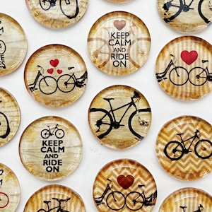 May include: Assortment of 10 round glass cabochons with various bicycle designs. The designs include a bicycle with a heart, a bicycle with the text "Keep Calm and Ride On", and a bicycle with a chevron pattern. The cabochons are approximately 2.5 cm in diameter.