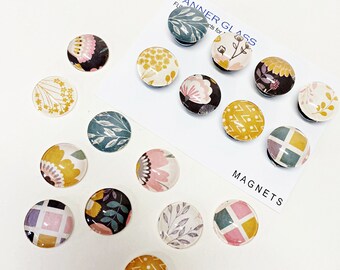 May include: A collection of decorative magnets with floral and geometric patterns. The magnets feature various designs in colors like yellow, pink, teal, and black. The text "Magnets" is visible on a white card, along with the text "TANNER GLASS".