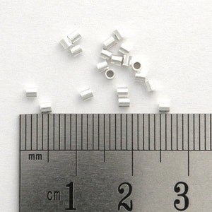 May include: A close-up of a ruler with silver jump rings scattered on a white surface. The ruler measures in centimeters and inches. The jump rings are approximately 3 mm in diameter.
