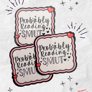 May include: Three stickers with a white background and a pink border. The text "Probably Reading SMUT" is written in black script. Each sticker has a red heart and small black hearts. Decorative starbursts and stars surround the stickers.