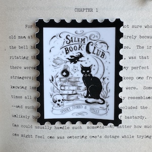 May include: A black and white sticker with a Salem Book Club design. The sticker features a black cat, a witch on a broom, a stack of books, a skull, and the words "Spooky Stories & Spells."