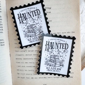 May include: Two black and white stickers with a vintage stamp design. The stickers feature a stack of books, bats, and the text "Proud Member of the Haunted Readers Society".