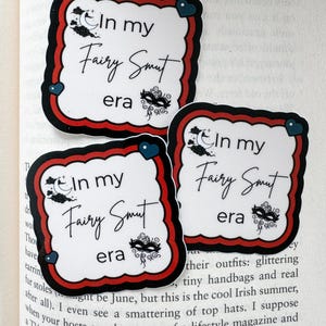 May include: Three stickers with a white background and a black and red border. The stickers have the text "In my Fairy Smut era" in black script, with a crescent moon and mask graphic.