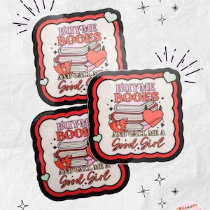 May include: Three stickers with a white background, black and red border, and the text "BUY ME BOOKS" and "AND CALL ME A Good Girl". The stickers feature a stack of books, a heart, and a small devil.