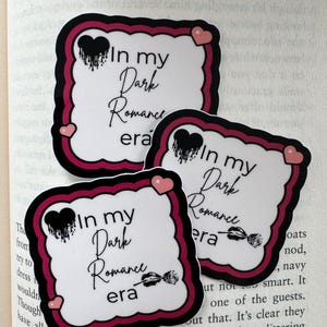 May include: Three square stickers with the text "In my Dark Romance era". The stickers have a white background with a black and cerise border. Each sticker has a black heart with dripping paint and a cerise heart.