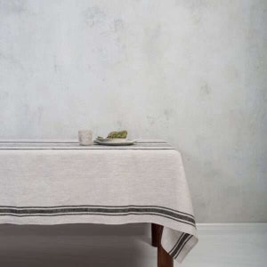Peut inclure: Une nappe en lin blanc avec des rayures noires. La nappe est drapé sur une table en bois et a un aspect simple et rustique.