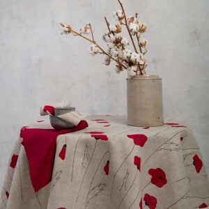 May include: A round tablecloth with a beige background and a red poppy flower design. A red napkin and a small bowl are on the table. A beige ceramic vase holds cotton branches.